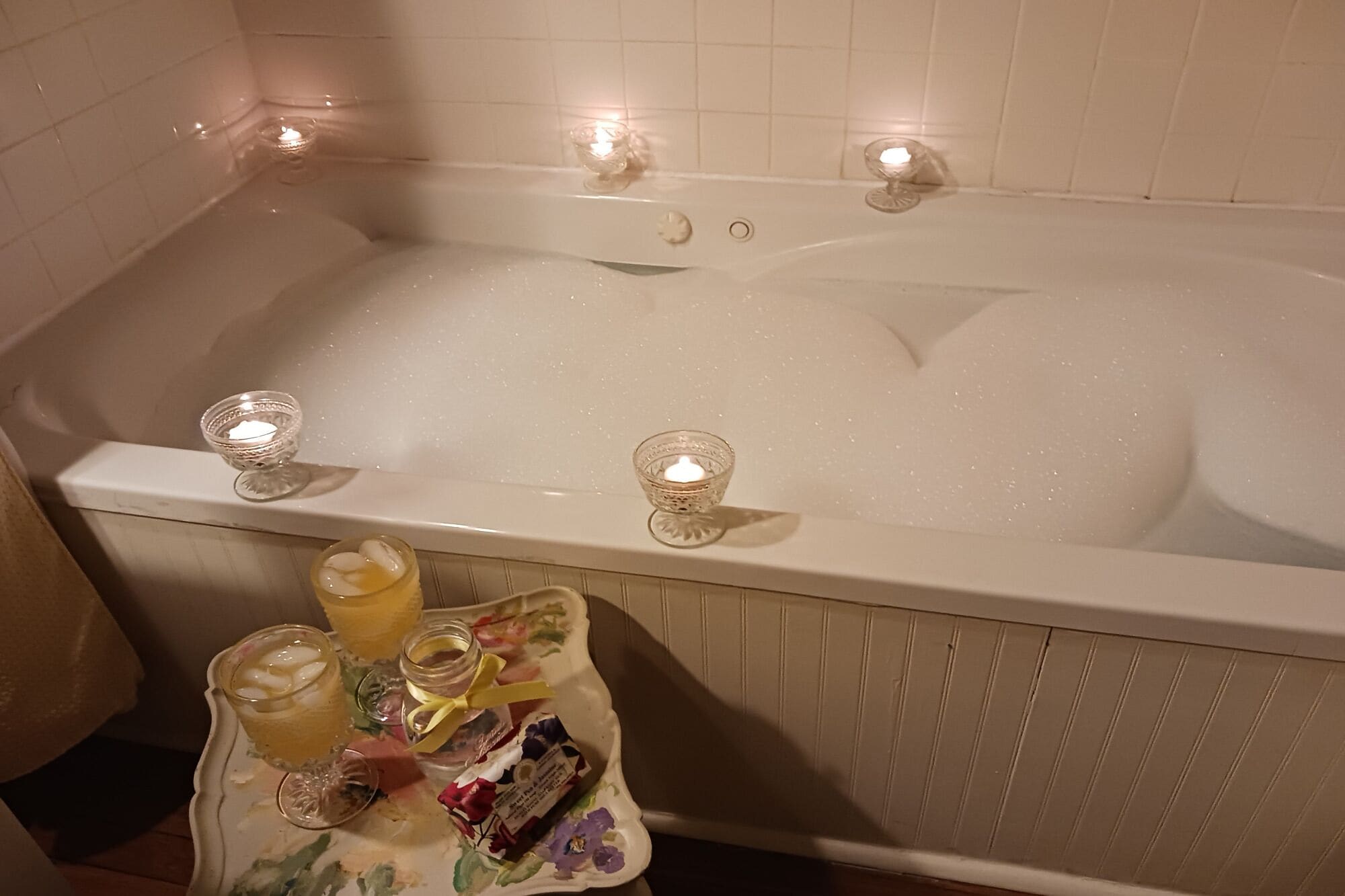 Eine Badewanne mit zwei brennenden Kerzen und einem Tablett mit einer Flasche und einem Glas.