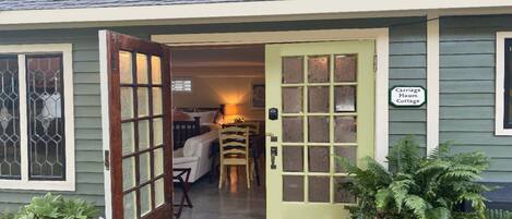 A cottage with a green exterior, a wooden door with glass panels, and a sign indicating it's a carriage house.