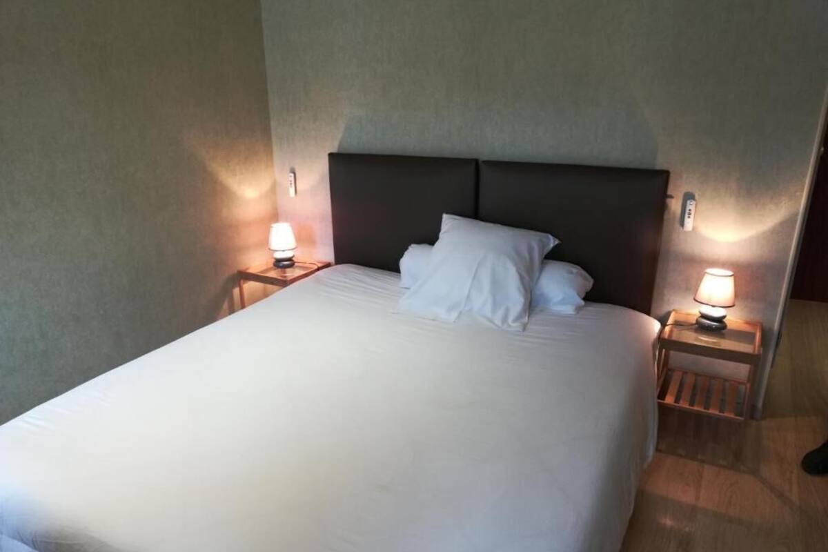 A hotel room with a large bed, two bedside tables with lamps, and a headboard.