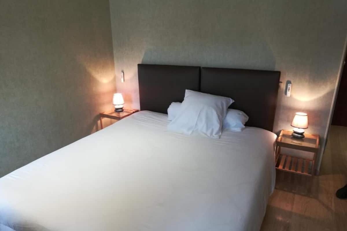 Una habitación de hotel con una cama grande, dos mesitas de noche con lámparas y un cabecero.