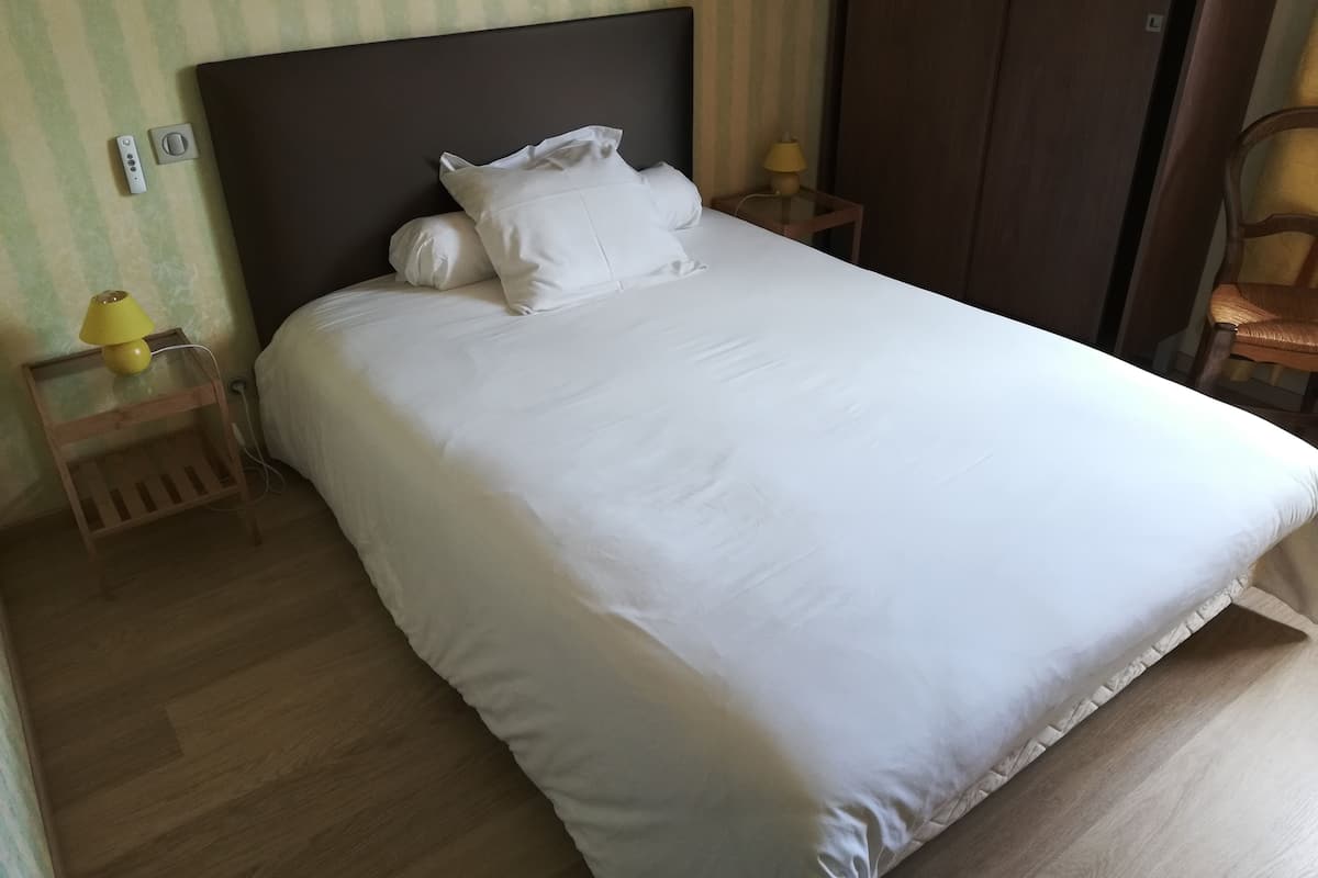 A neatly made bed with white bedding, a wooden nightstand with a lamp, and a chair.