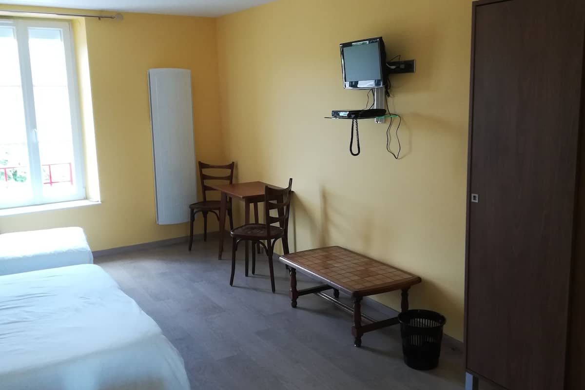 A hotel room with two beds, a desk, a chair, a TV, and a wardrobe.