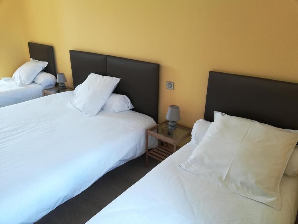 Een hotelkamer met twee bedden, elk voorzien van witte beddengoed en een donker hoofdeinde. Daartussen staat een klein tafeltje met een lamp.