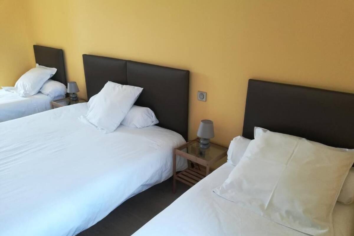 A hotel room with two beds, each with white bedding and a dark headboard. There is a small table with a lamp between the beds.