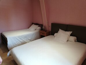 Deux lits simples avec du linge de lit blanc, dans une chambre aux murs roses.