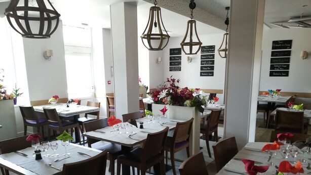 A restaurant with multiple tables set for dining, featuring a modern interior with pendant lighting and a menu board on the wall.