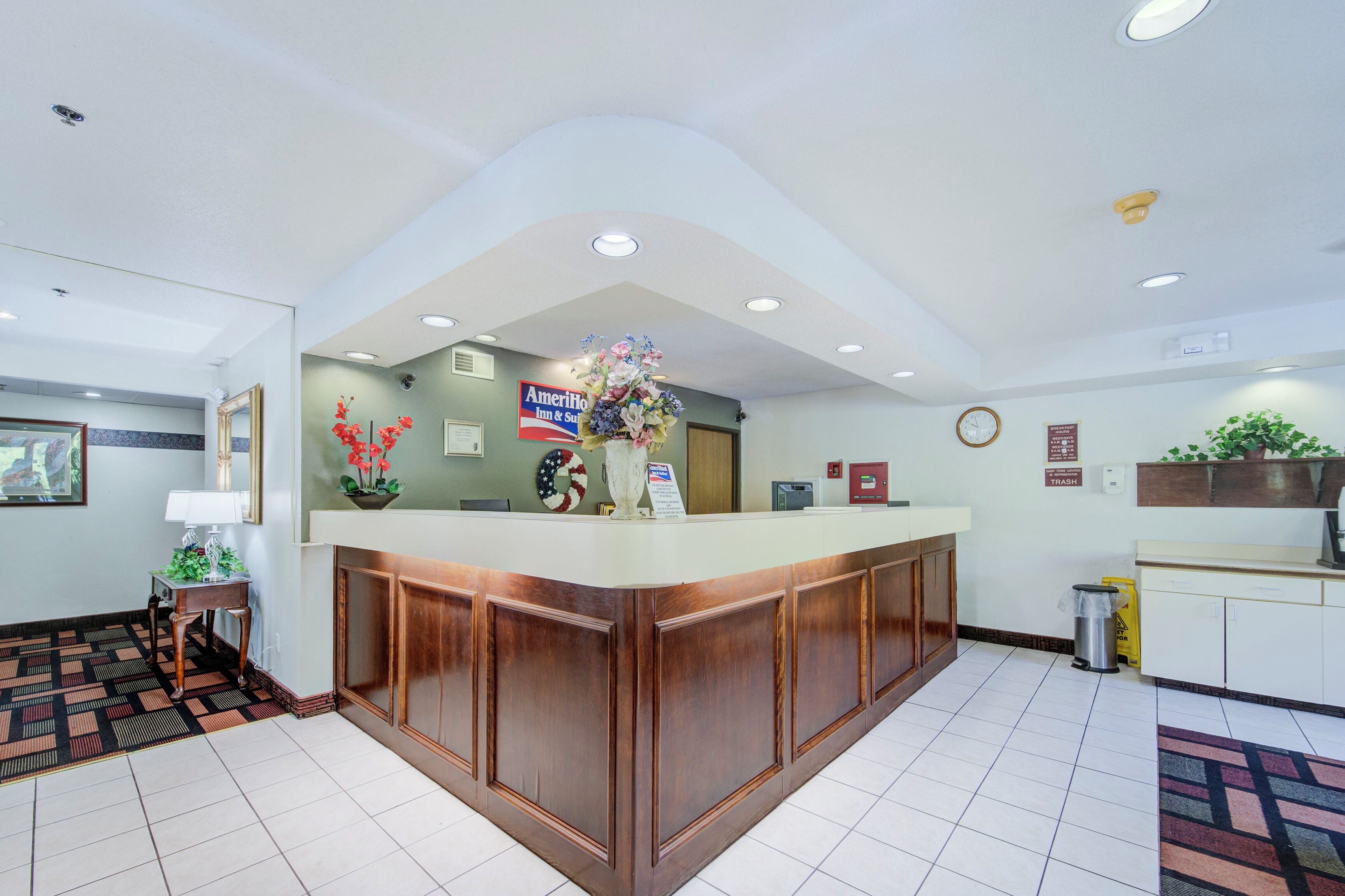 Un espace d’accueil avec un comptoir de réception en bois, une horloge et une enseigne indiquant « AmeriHo Inn & Suites ».