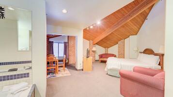 A hotel room with a bed, a chair, a desk, a mirror, and a bathroom with a bathtub and sink.
