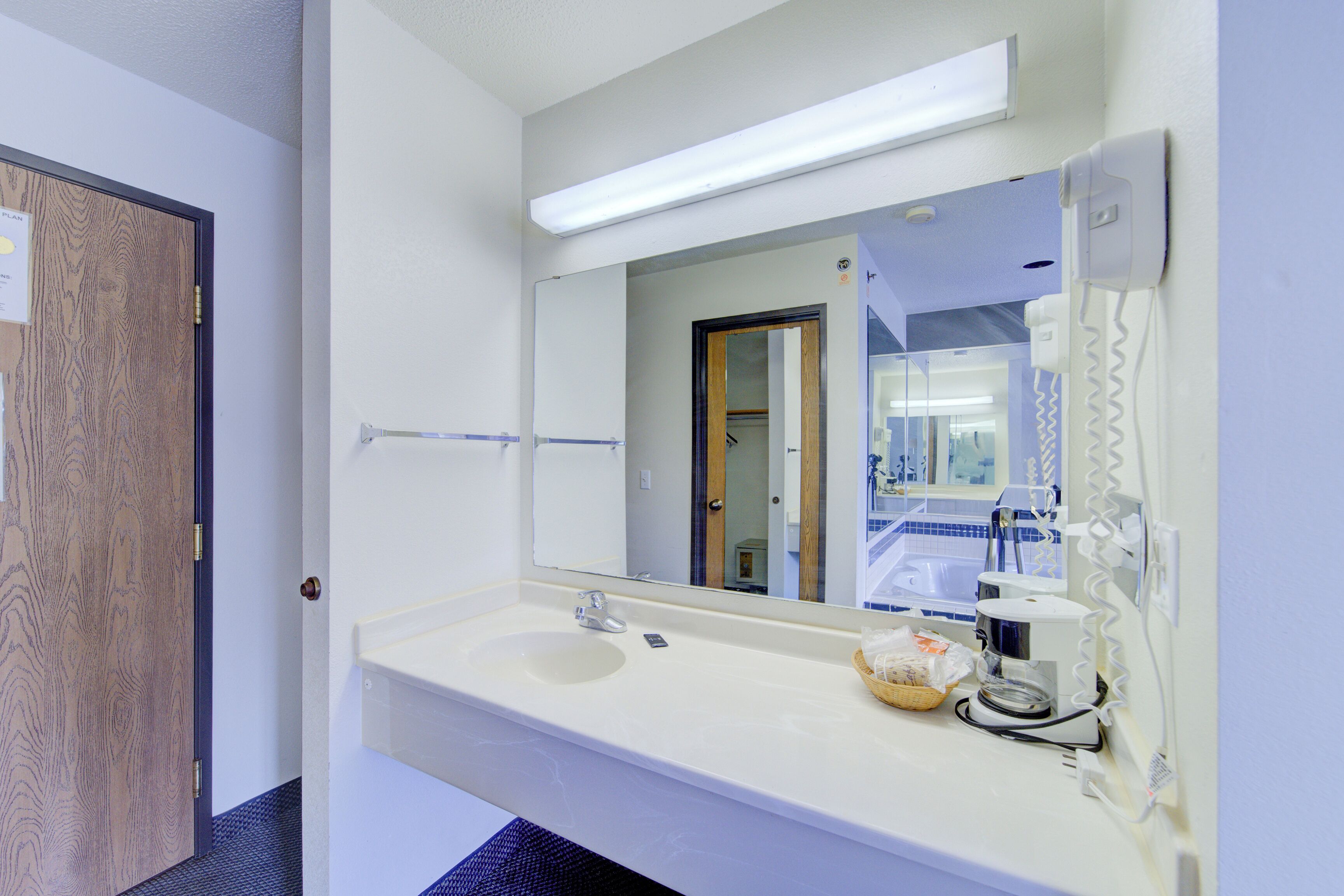 Une salle de bain d’hôtel avec un lavabo blanc, un miroir, une machine à café et un porte-serviettes.