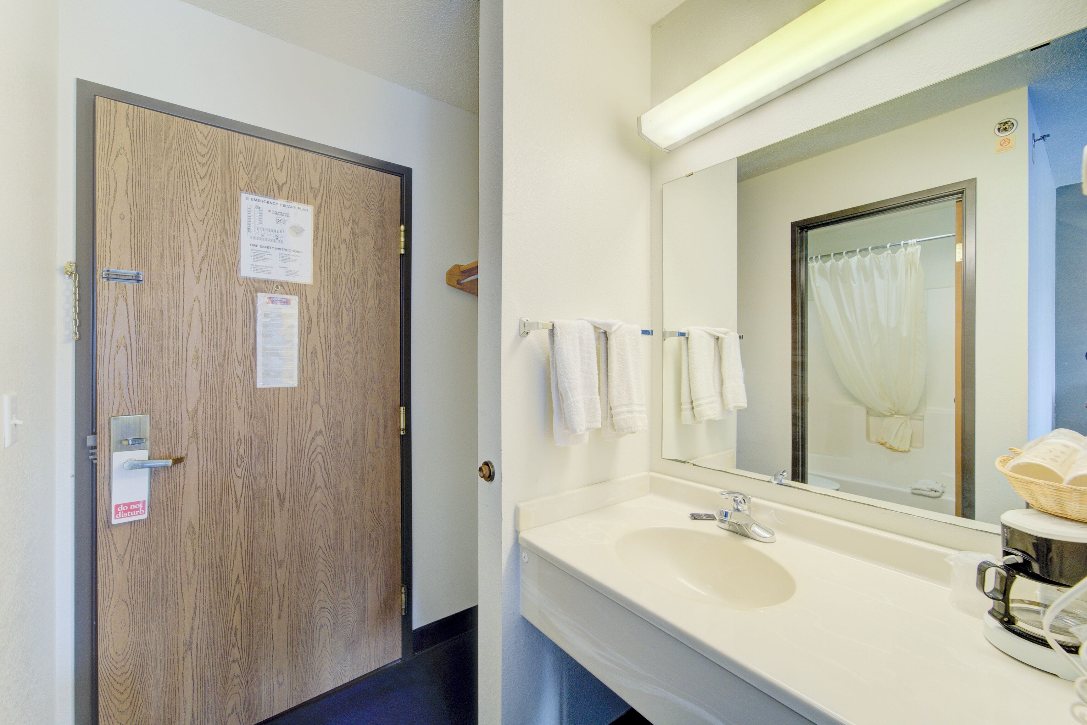 Un baño de hotel con puerta de madera, lavamanos, espejo y toallero.
