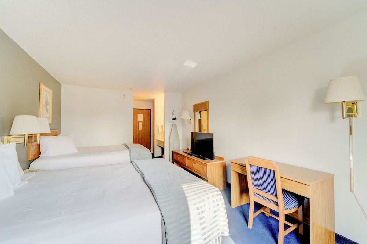A hotel room with a bed, a desk, a chair, a television, and a lamp.