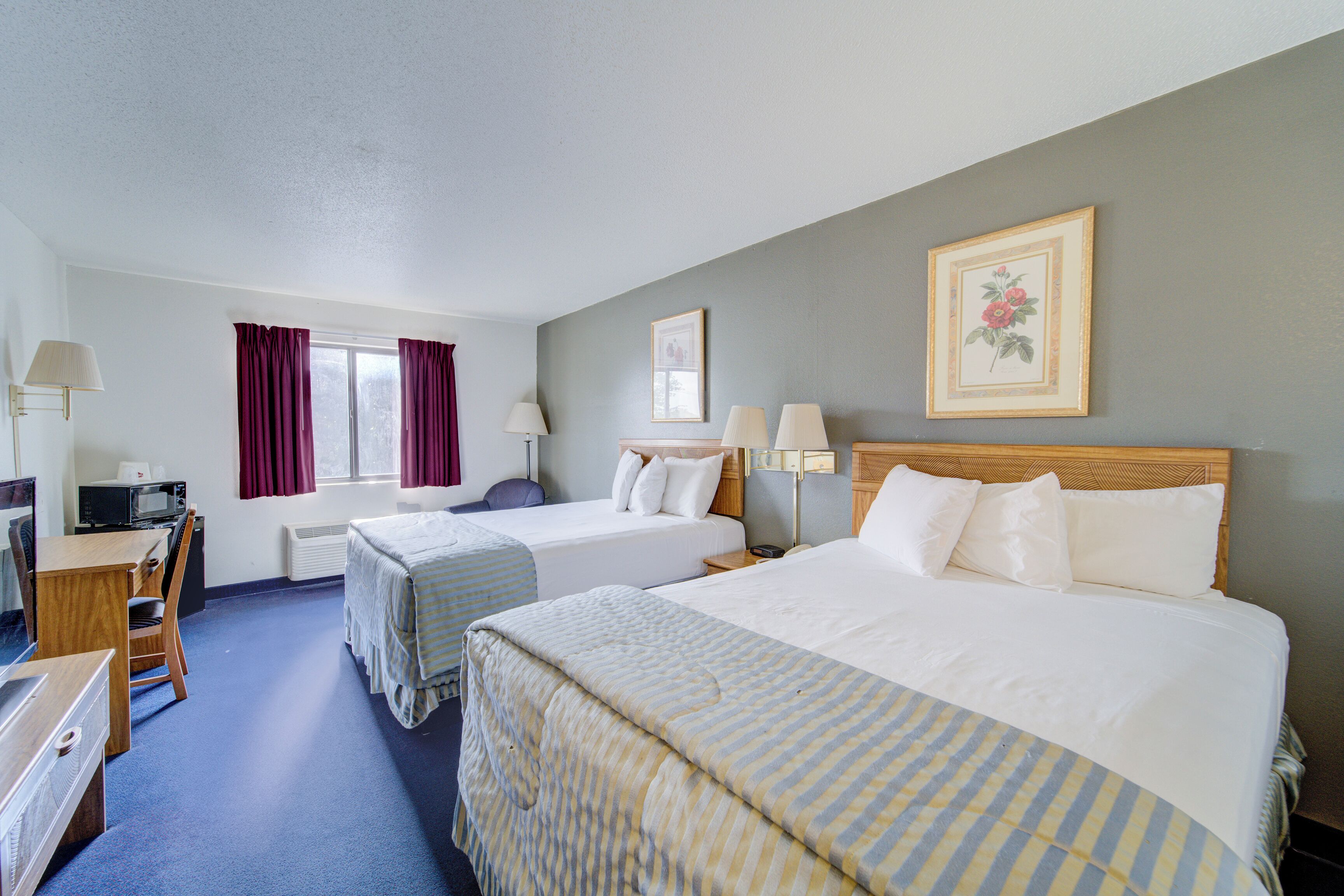 A hotel room with two beds, a desk with a chair, a microwave, and a window with curtains.
