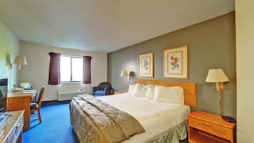A hotel room with a large bed, a desk with a chair, a window with curtains, and two wall-mounted lamps.