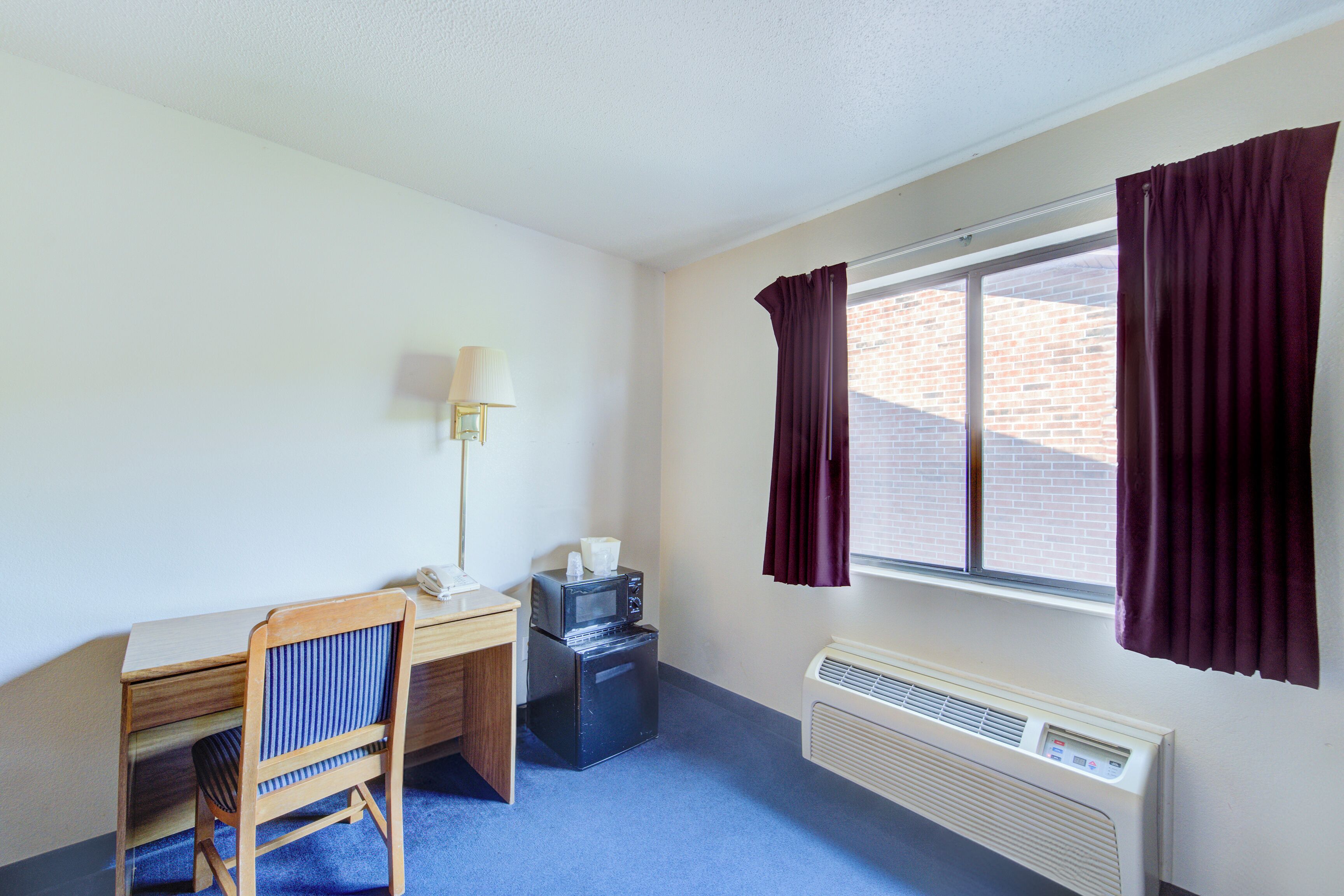 A small room with a desk, chair, microwave, and heater.