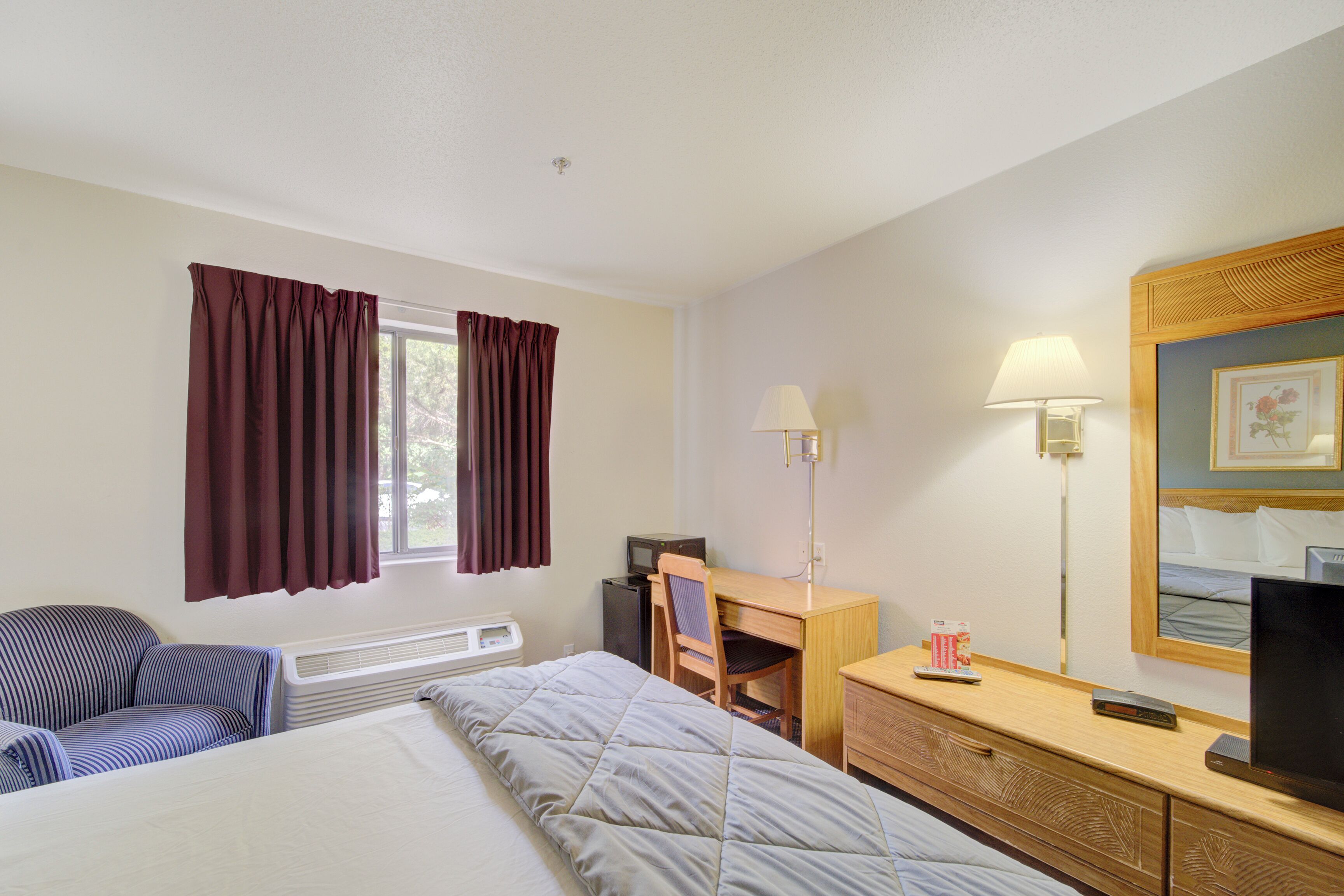 Habitación de hotel con cama, escritorio, silla, televisor y lámpara.