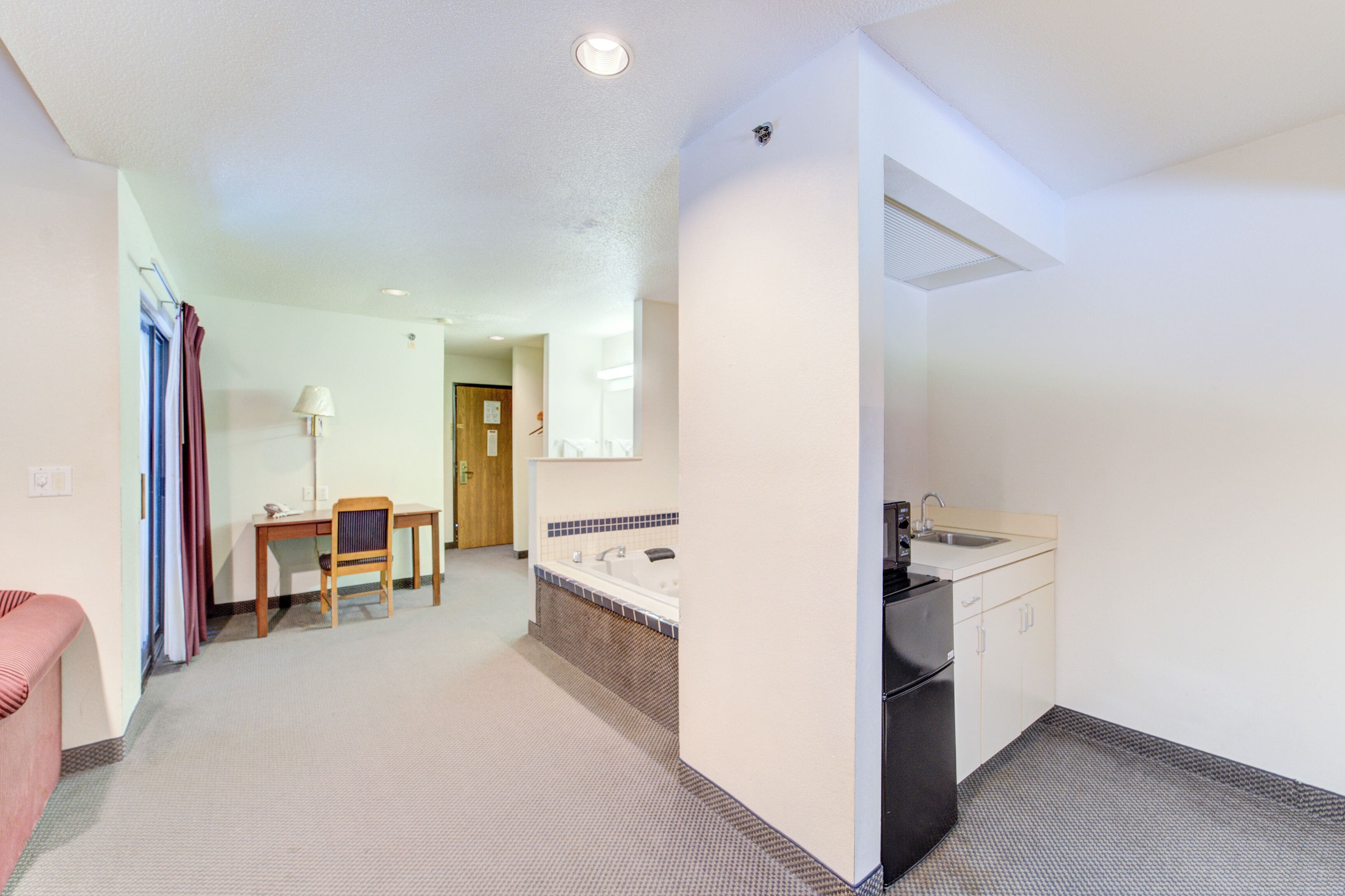 A hotel room with a kitchenette, a small dining area, and a bathroom with a bathtub.