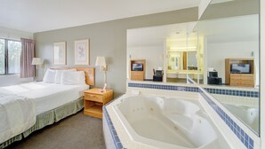A hotel room with a large bed, a sitting area with a chair and table, a large bathtub, and a mirror reflecting the room. - Capital O Amerihost Inn and Suites Fulton Hwy 54 MO (Fulton)