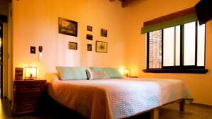 Un dormitorio con cama, dos mesitas de noche, una ventana con vistas y varias fotografías enmarcadas en la pared.