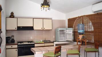 Cocina pequeña con estufa, pileta y refrigerador. Hay dos sillas con cojines verdes y una mesa.