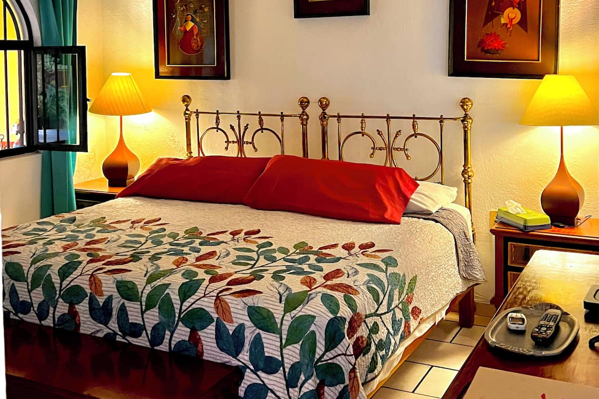 A hotel room with a bed, two bedside lamps, a ceiling fan, and three framed pictures on the wall.