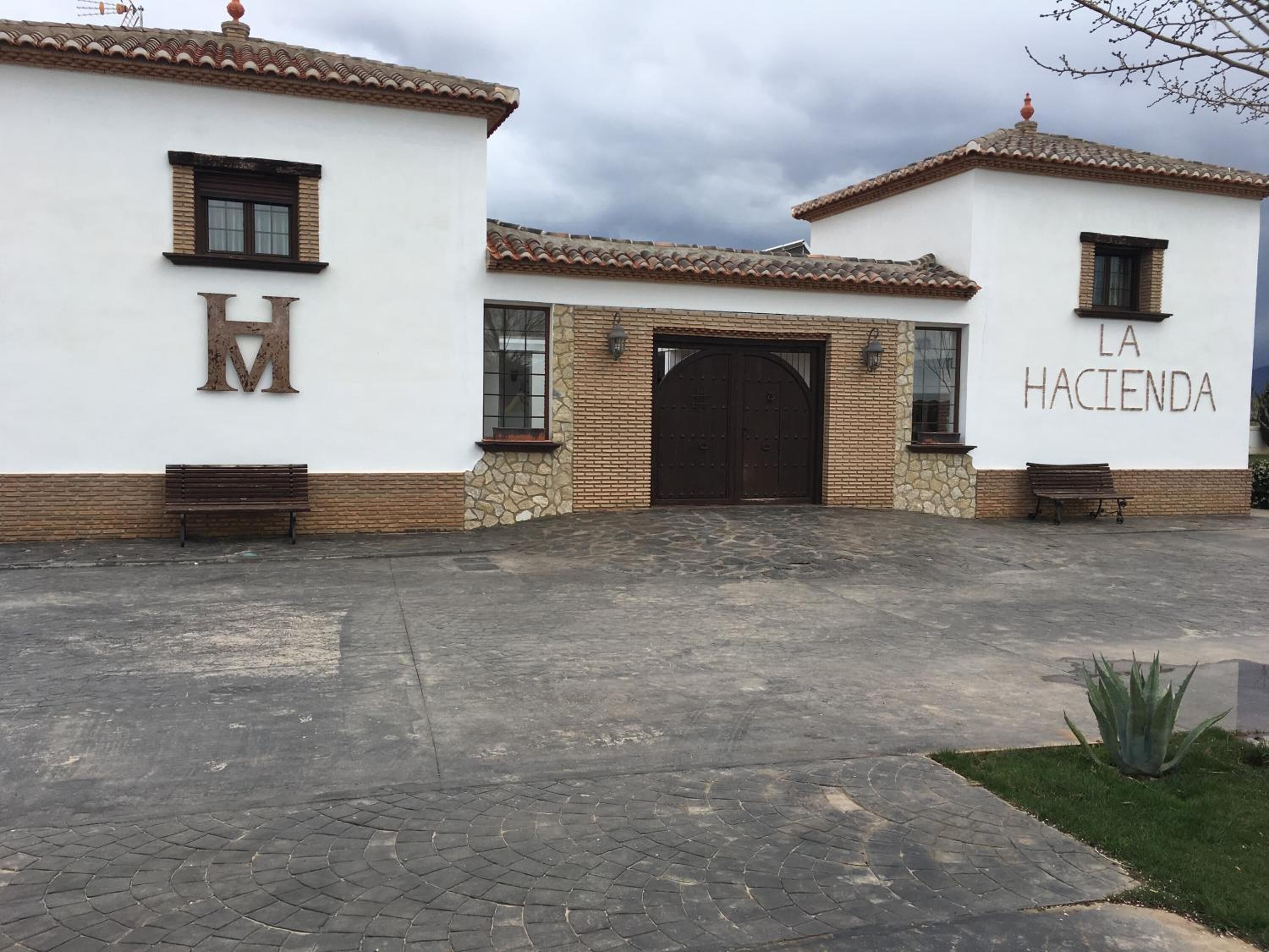 Edifici amb un gran 'H' metàl·lic i un rètol que diu 'La Hacienda', una entrada de pedra i bancs.