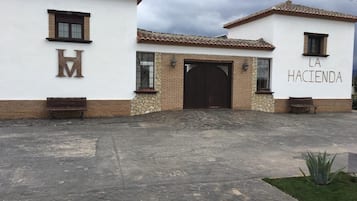 Un bâtiment avec un grand « H » en métal et une enseigne « La Hacienda », une entrée en pierre et des bancs.