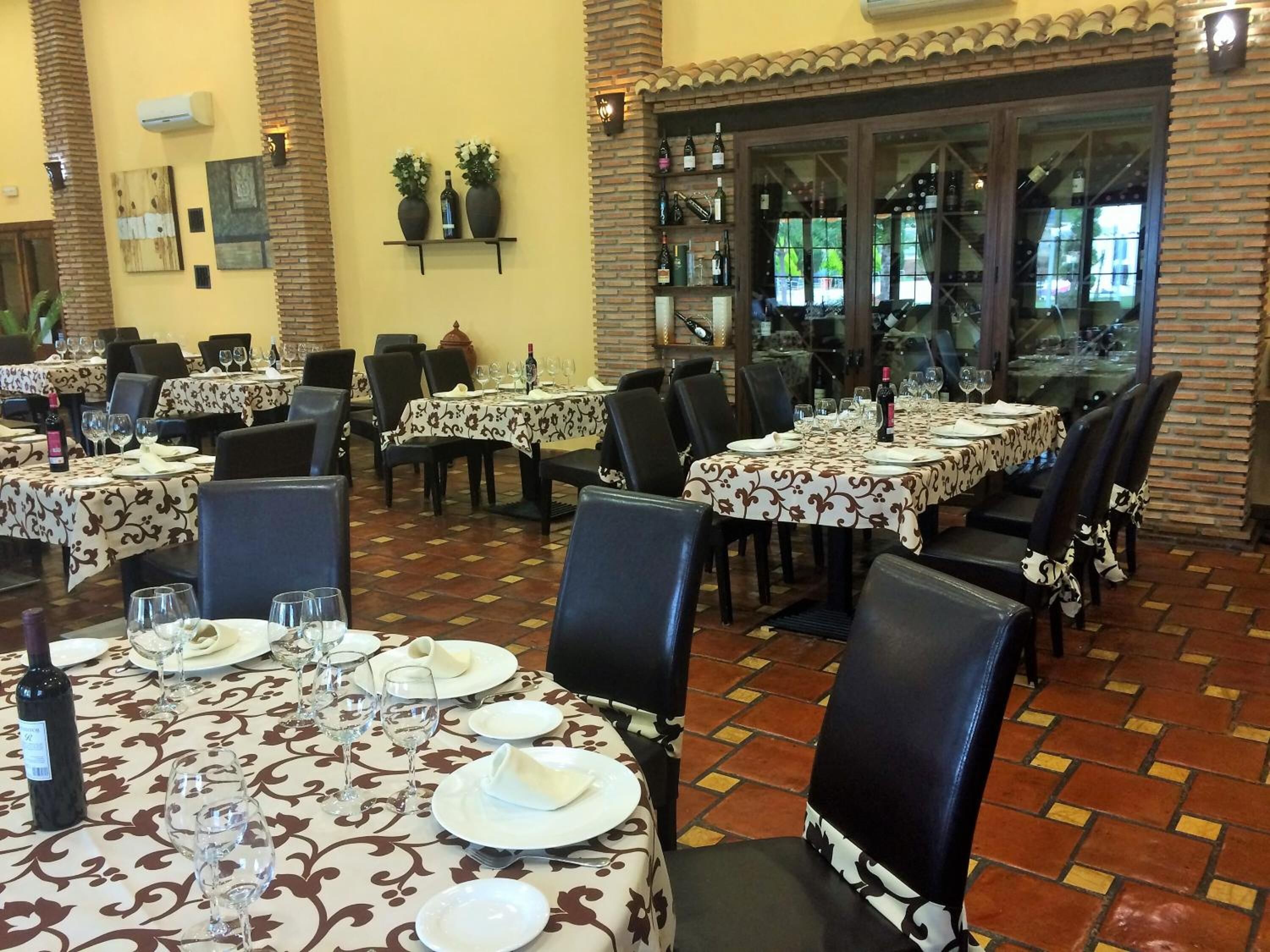 A restaurant with multiple tables set for dining, featuring patterned tablecloths and black chairs.