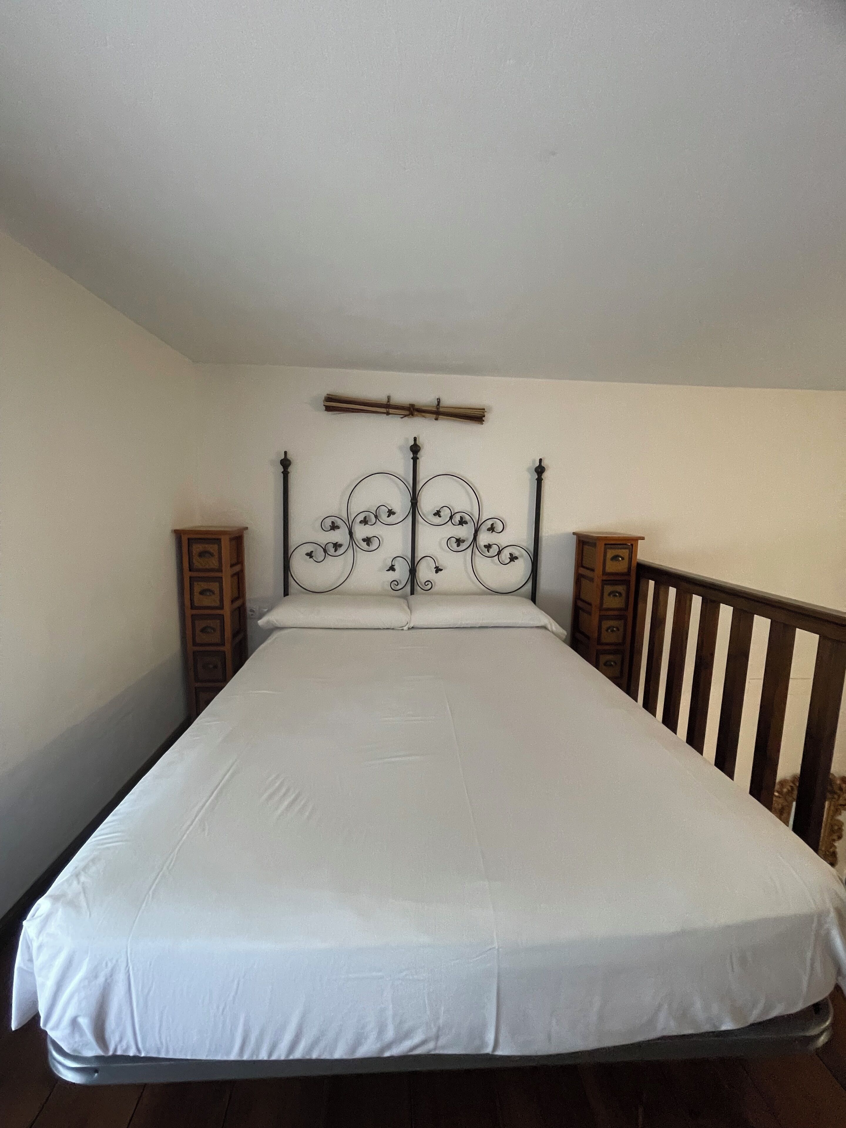 Une chambre avec un lit simple, une tête de lit en métal, des tables de chevet en bois et une balustrade en bois.