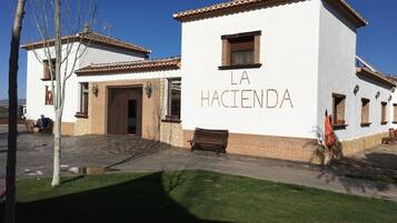 A building with the sign "LA HACIENDA" on its facade, featuring a traditional architectural style with a tiled roof and stone accents.