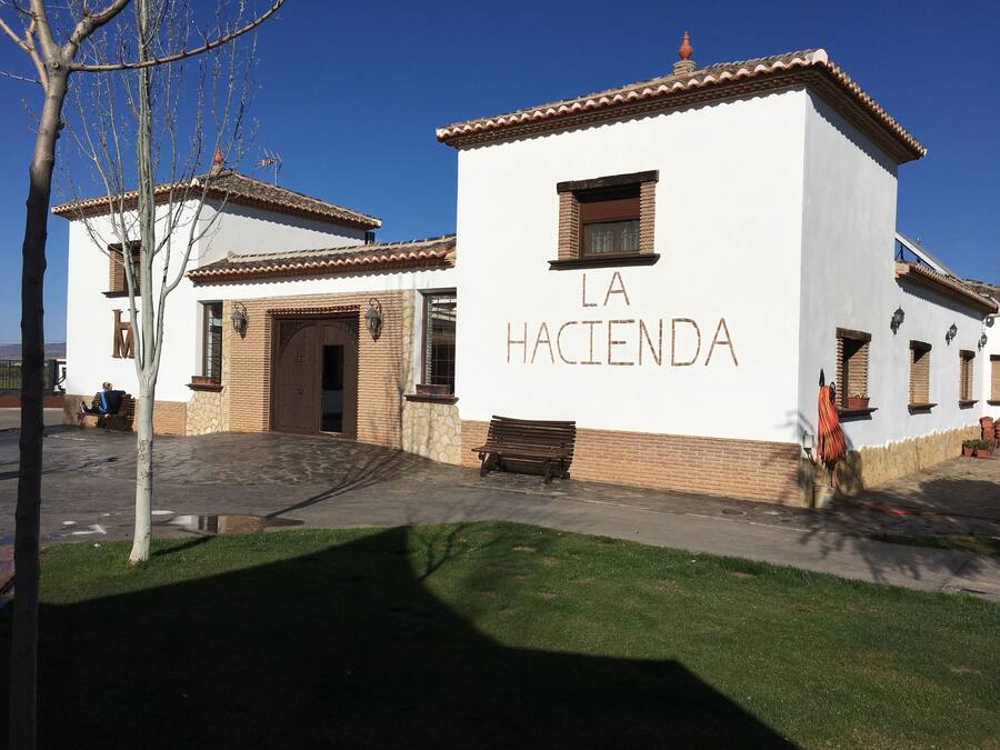 A building with the sign "LA HACIENDA" on its facade, featuring a traditional architectural style with a tiled roof and stone accents.
