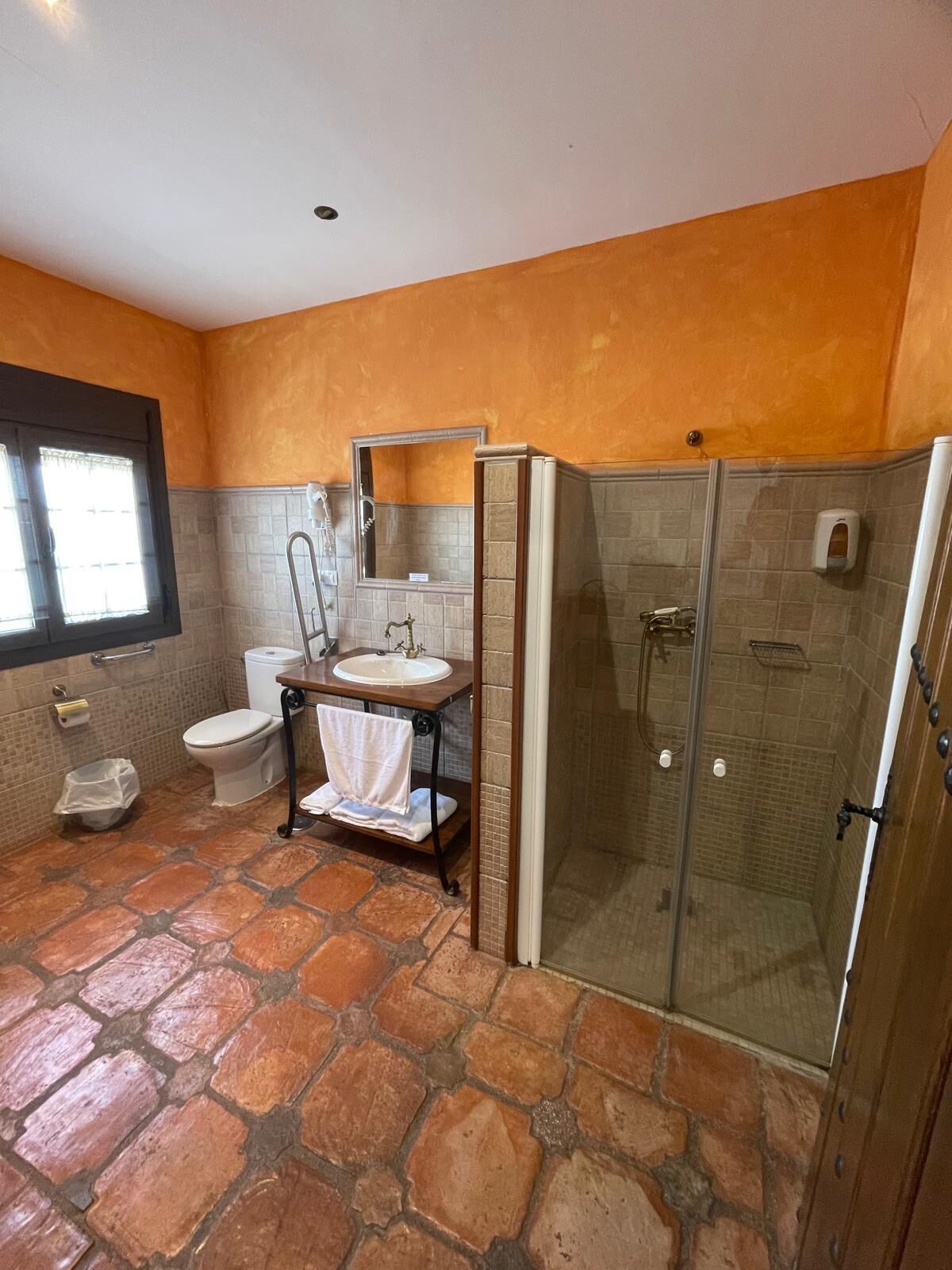 Een badkamer met een stenen vloer, toilet, wastafel met spiegel en een douche met glazen wanden.