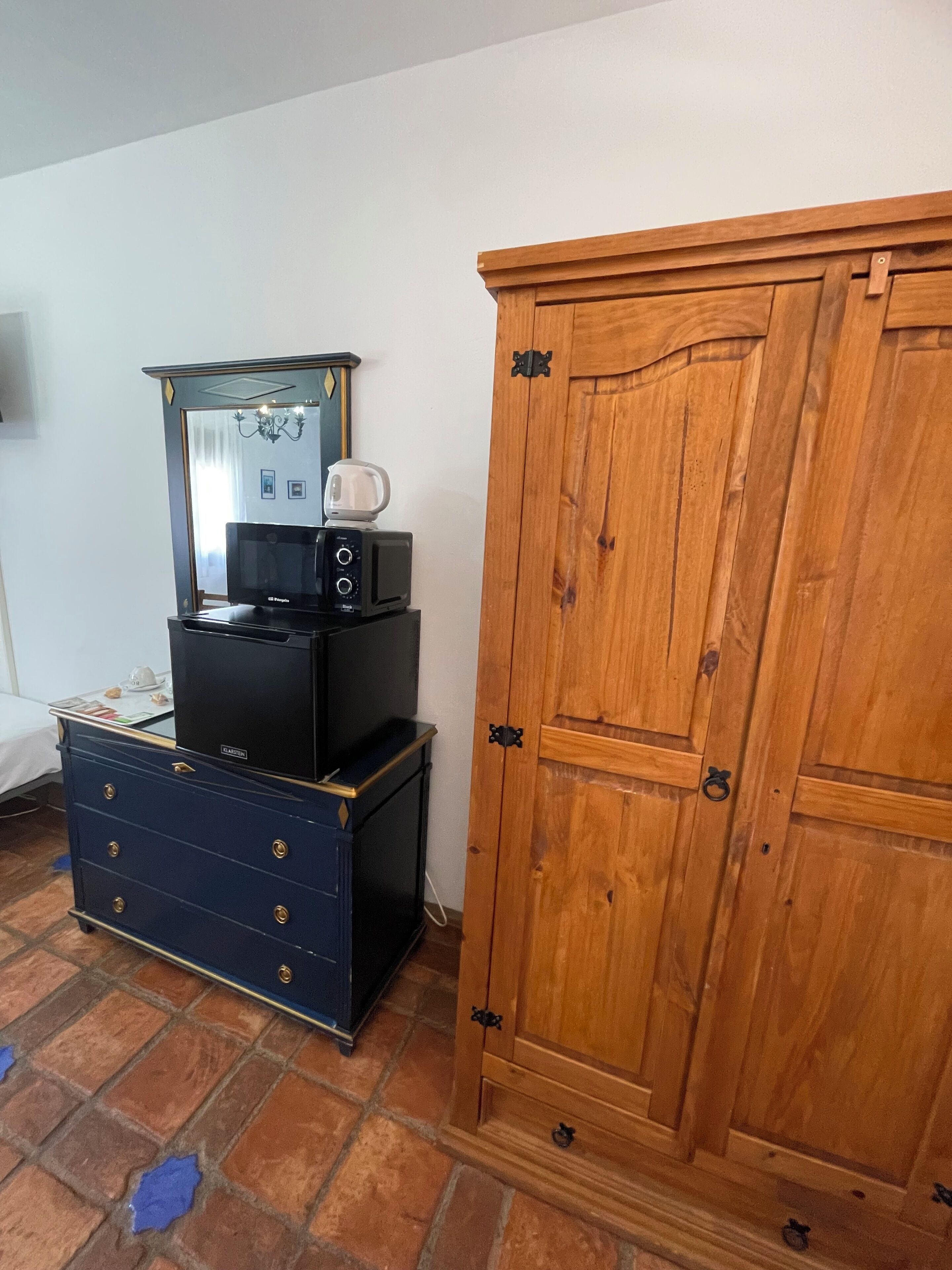 Una habitación con un armario de madera, un aparador negro, un espejo y un microondas sobre el aparador.
