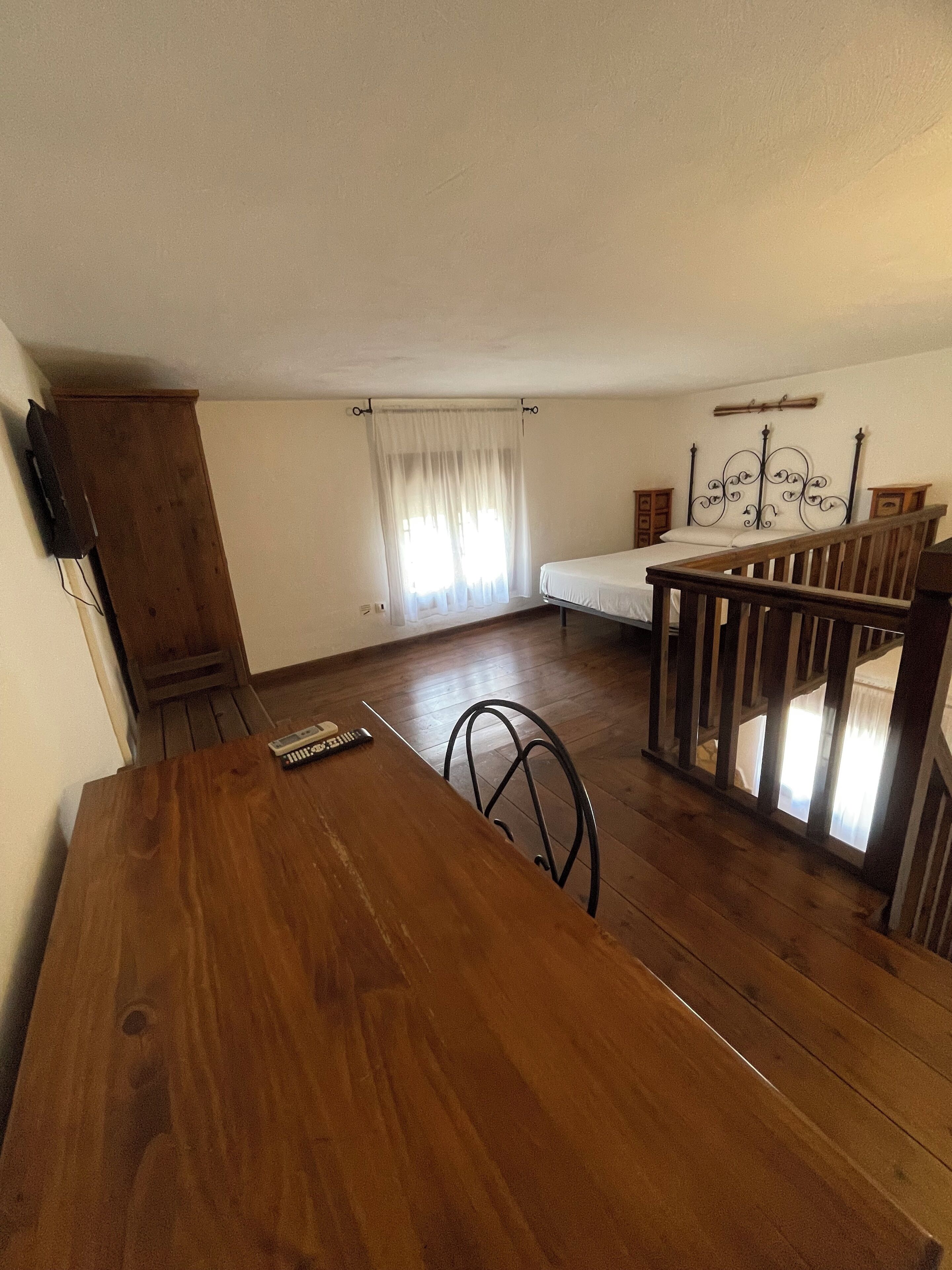 A room with a wooden dining table, a bed with a metal headboard, and a window with curtains.