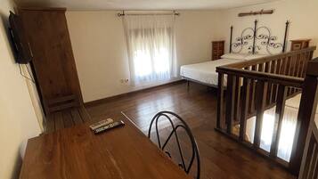 A room with a wooden dining table, a bed with a metal headboard, and a window with curtains.