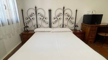 Un dormitorio con una cama grande, un escritorio, una silla, un televisor y un equipo de aire acondicionado en la pared.
