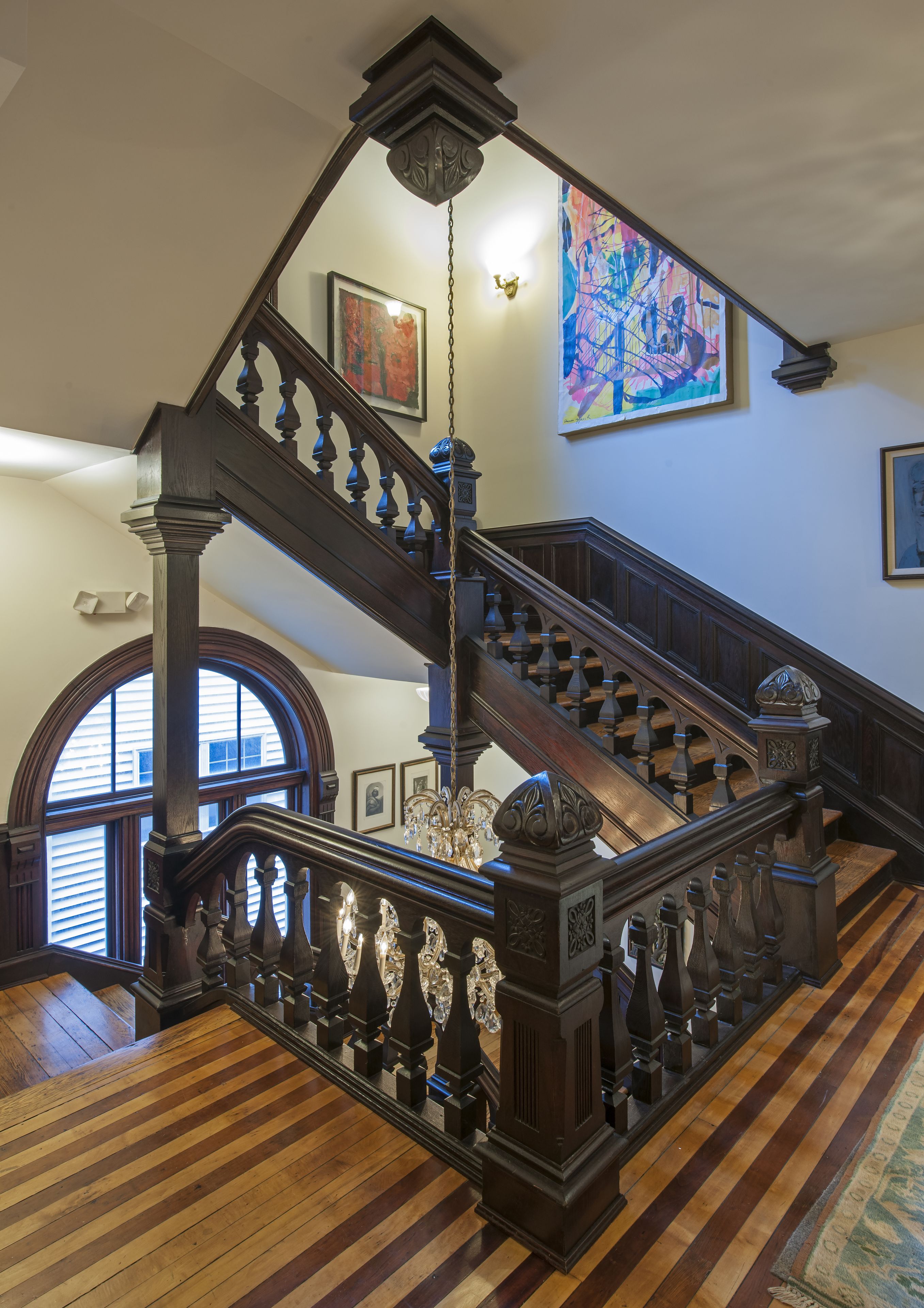A grand wooden staircase with intricate balusters and a chandelier, leading to an upper floor.