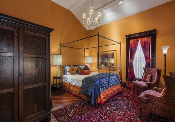 A four-poster bed with a patterned bedspread, a large wooden wardrobe, a chandelier, and a patterned rug. - The Inn at 97 Winder (Detroit)