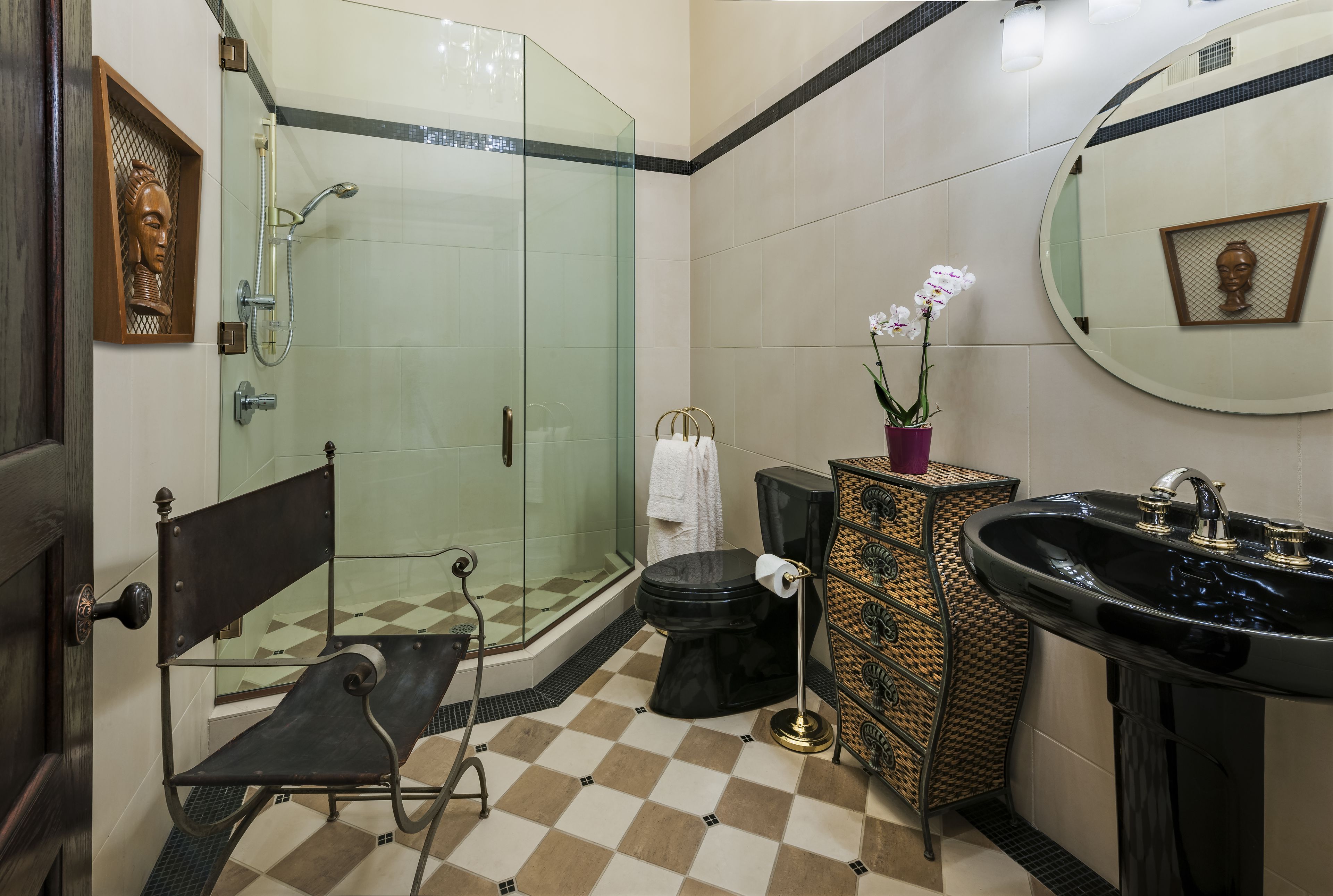 Une salle de bain dotée d’une douche à parois de verre, de toilettes noires, d’un lavabo noir et d’un meuble décoratif en osier.