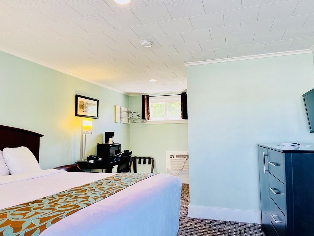 A hotel room with a bed, a desk with a computer, a dresser, and a window with curtains.
