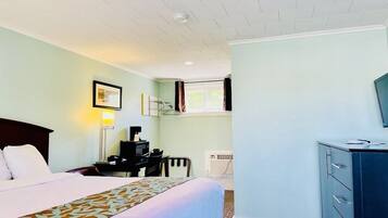 A hotel room with a bed, a desk with a computer, a dresser, and a window with curtains.