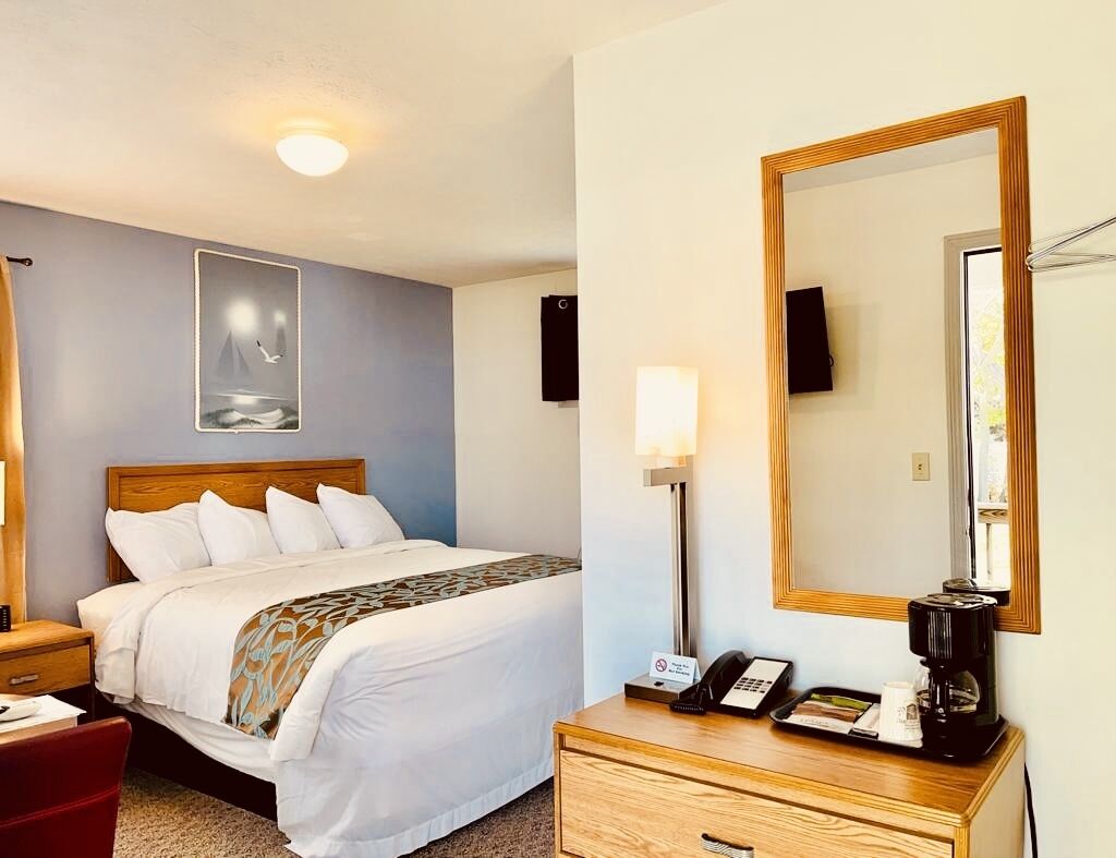 A hotel room with a bed, bedside table, lamp, and a large mirror.