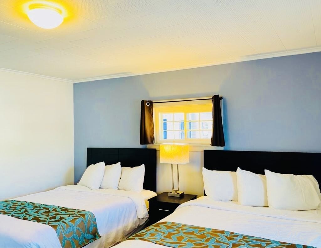 A hotel room with two beds, a window with curtains, a lamp, and a ceiling light.