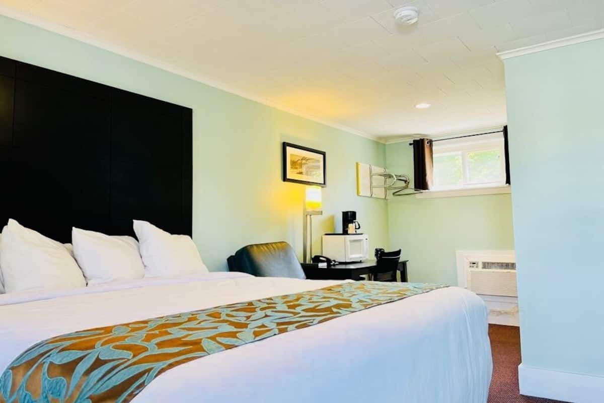 A hotel room with a bed, a desk, a chair, a lamp, and a window.