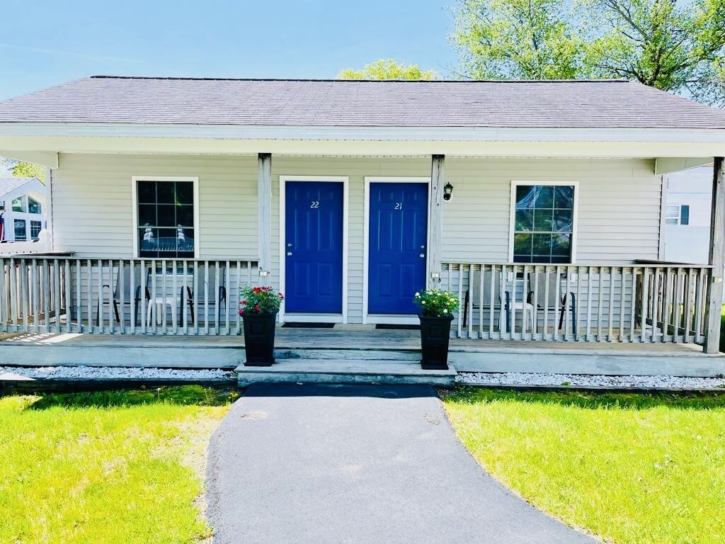 A two-story building with a white exterior and blue doors, featuring a covered porch with a railing and potted plants.