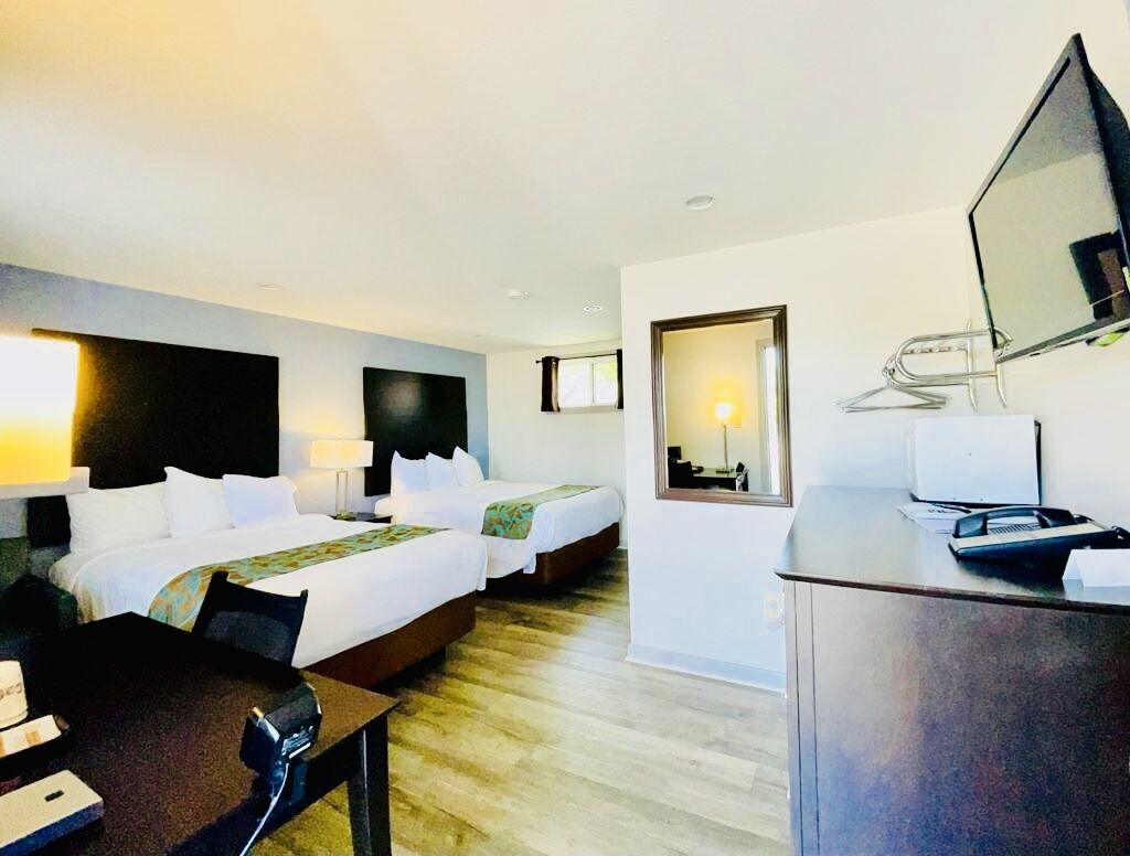 A hotel room with two beds, a desk, a chair, a TV, and a mirror.