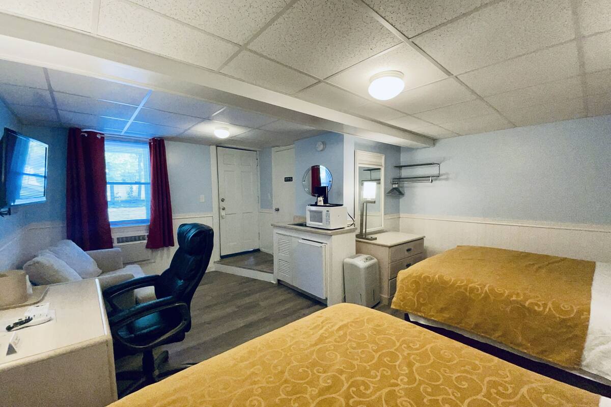 A hotel room with two beds, a desk, a chair, a microwave, and a television.