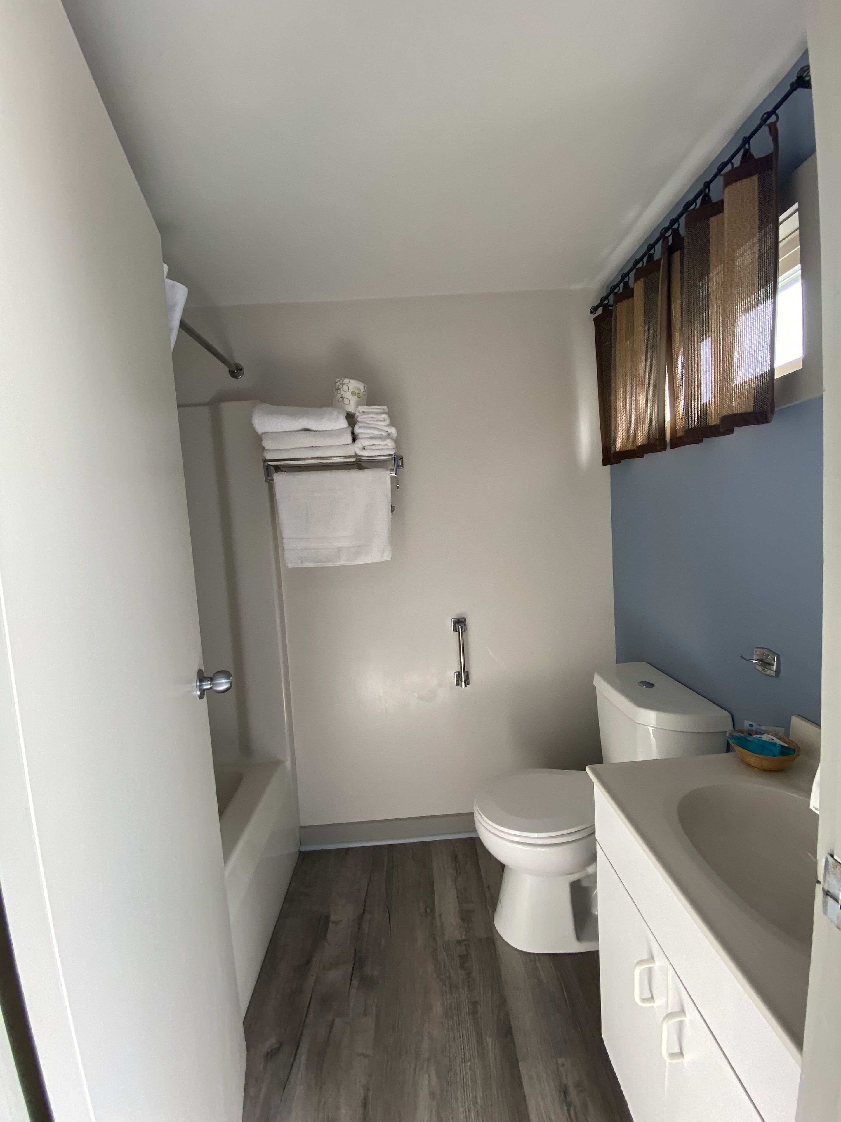A bathroom with a toilet, sink, and bathtub. There is a towel rack with towels and a toilet paper holder.