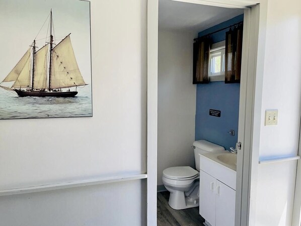 A bathroom with a toilet, sink, and a painting of a sailboat on the wall. - Wells Moody Motel (Wells)