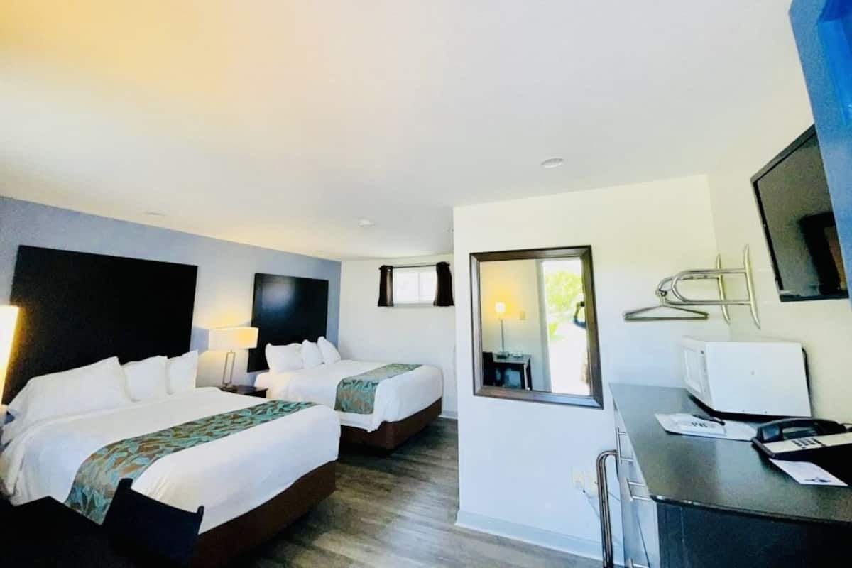 A hotel room with two beds, a desk with a computer, a mirror, and a window.