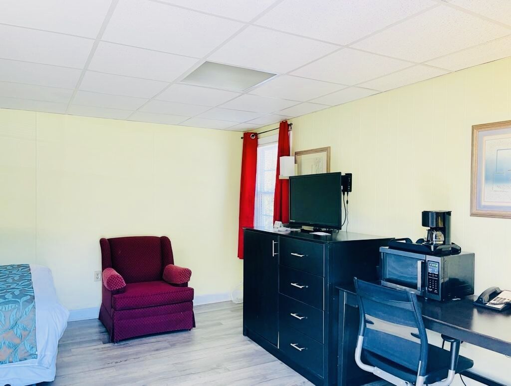 Une pièce comprenant un lit, un fauteuil rouge, un bureau avec un ordinateur, un four à micro-ondes et un téléphone.
